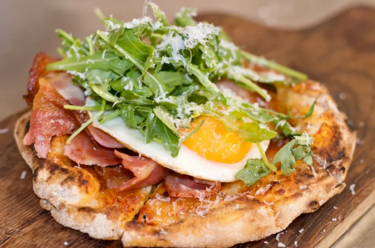 Breakfast pizza with bacon, fried egg, rocket and parmesan