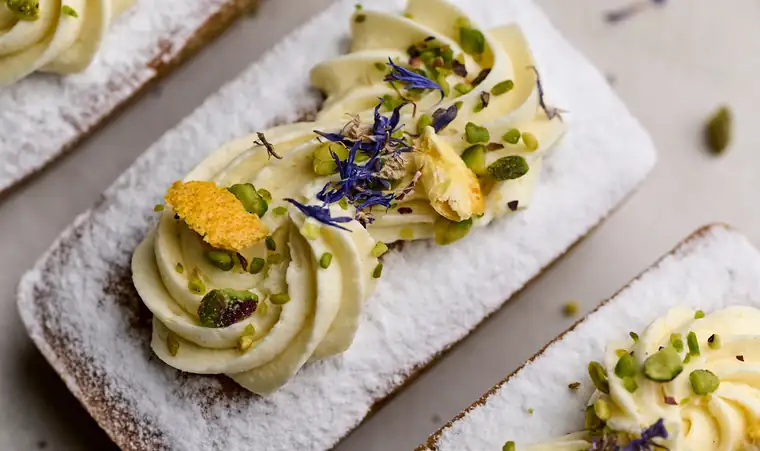 Mini loaf cakes with whipped cream, pistachio, citrus peel and cornflower petals